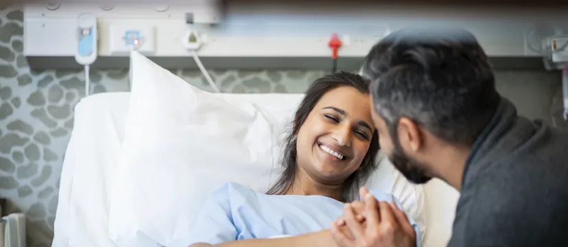 Smiling woman in a hospital bed holding hands with her partner